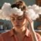 Woman touching her temple beside staged cotton cloud props in a kitchen.