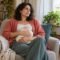 Woman seated in an armchair holding a covered hot water bottle against her clothed belly.